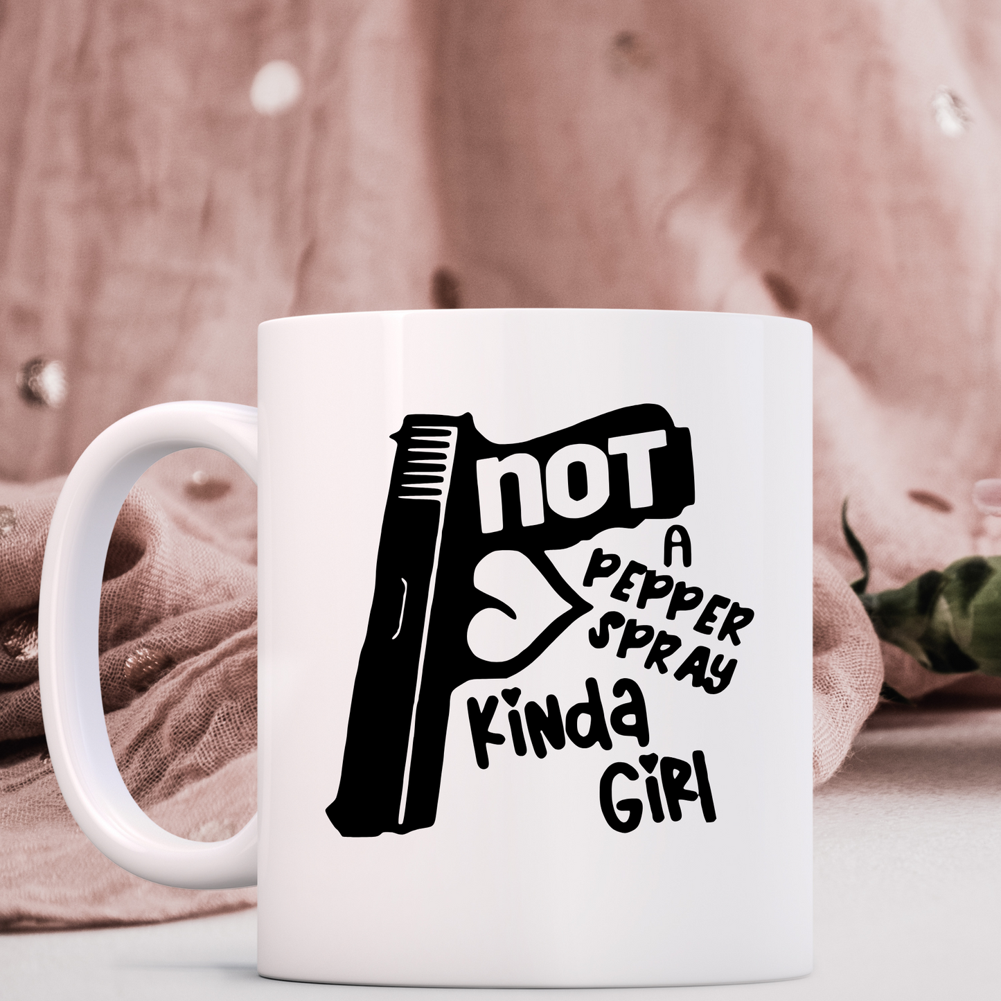 Black vinyl decal with a pistol that says not a pepper spray kinda girl on a coffee mug with a pink drape in the background