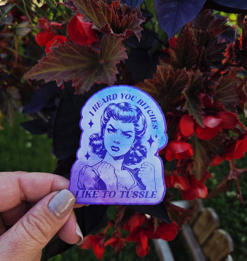 Sticker featuring a vintage-style woman with fists up and the phrase “I Heard You Bitches Like to Tussle” in purple and teal tones
