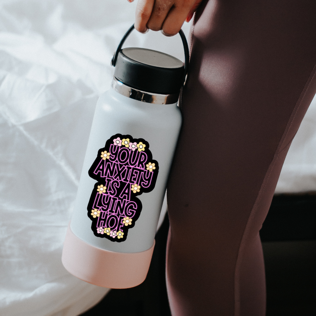 Holographic mental health sticker with the quote “Your Anxiety Is a Lying Hoe” in purple and white with flower doodles