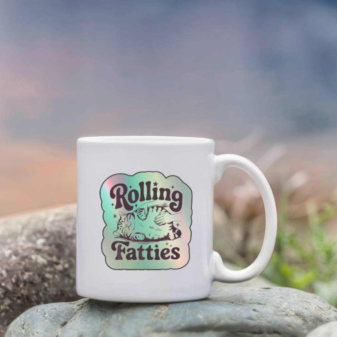 Holographic sticker with a hand rubbing a fat, relaxed cat and the phrase “Rolling Fatties” in playful black text