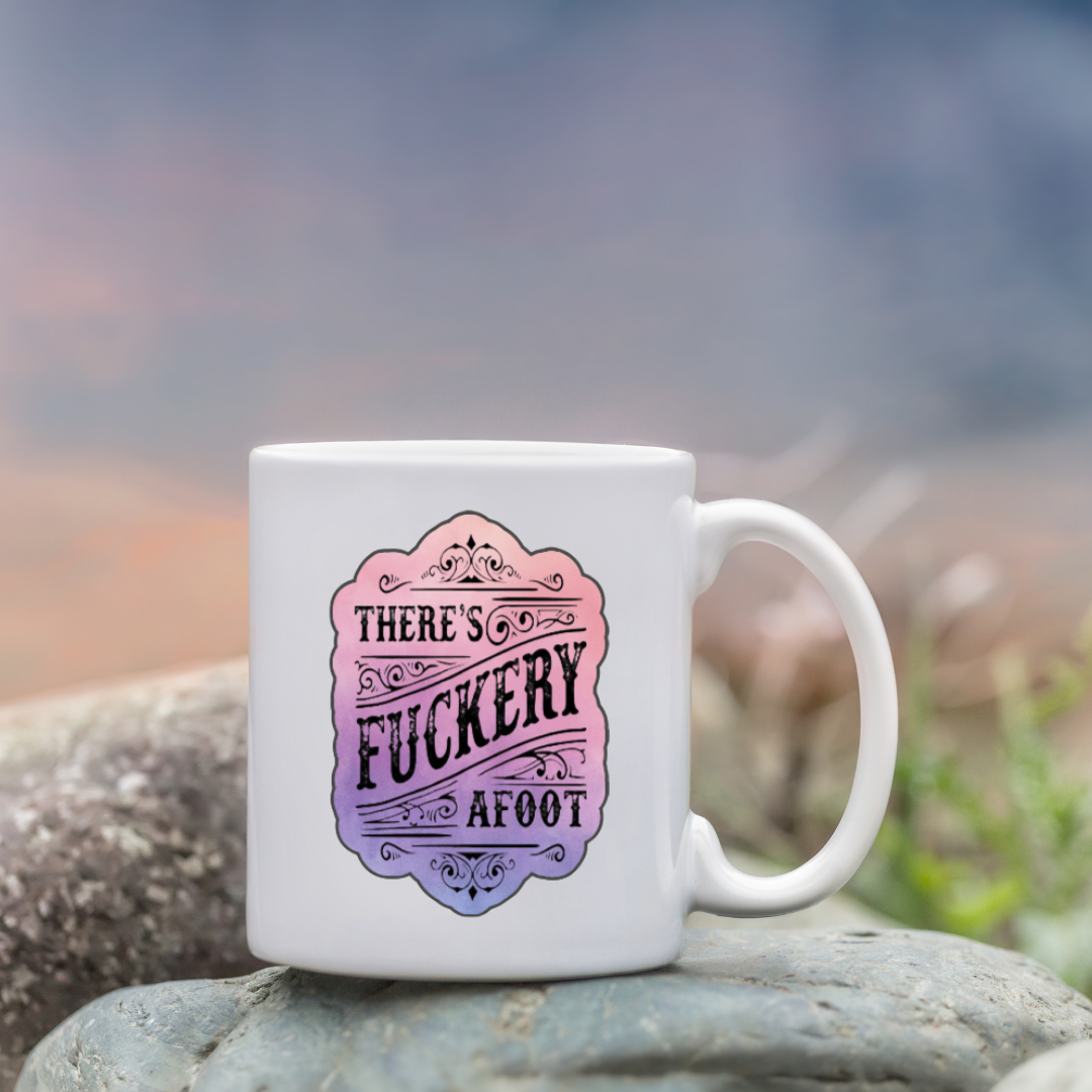 Sticker with ornate scrollwork and the phrase “There’s Fuckery Afoot” in black gothic-style lettering over a pink and purple gradient background