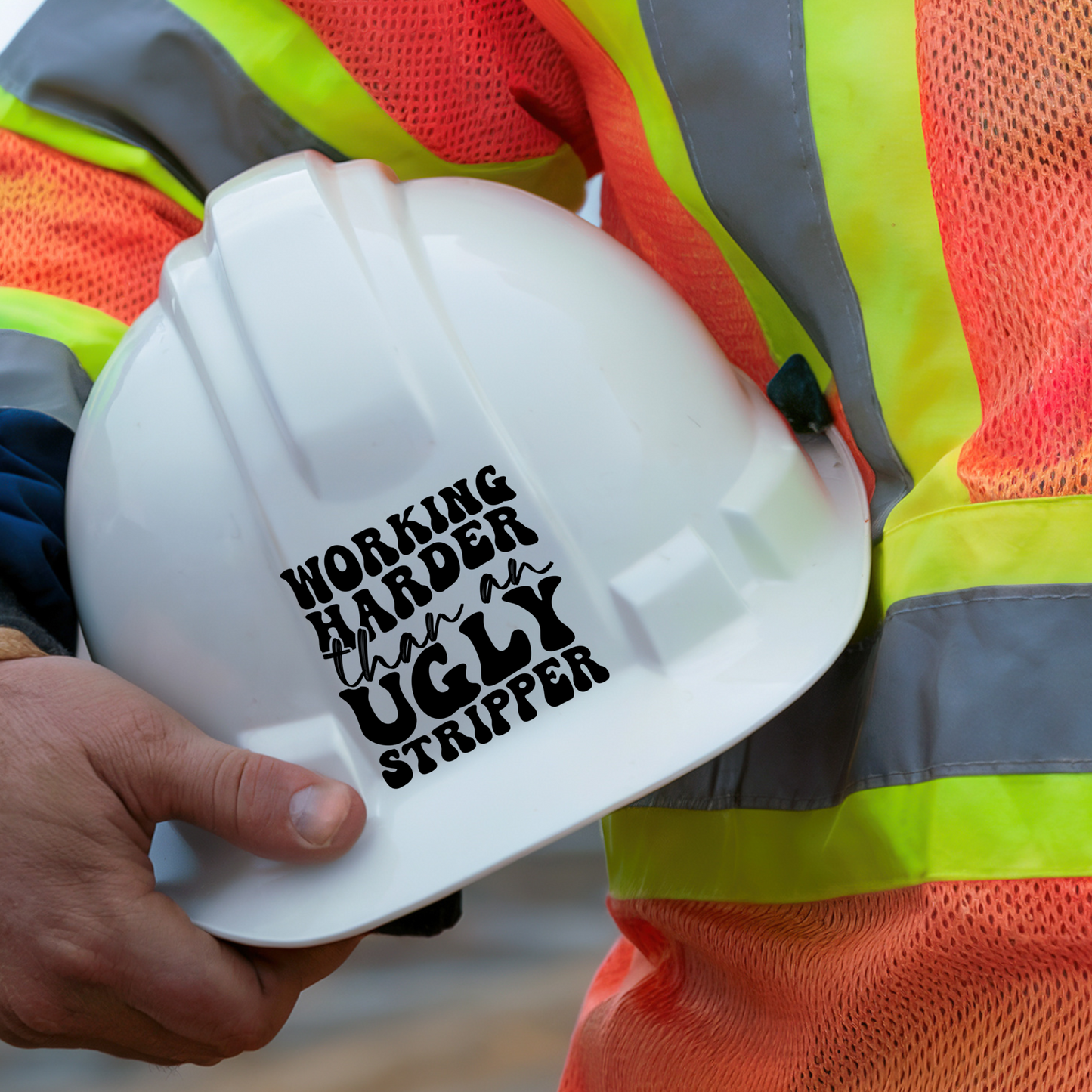 Construction worker holding a hard hat with a decal that says working harder than an ugly stripper