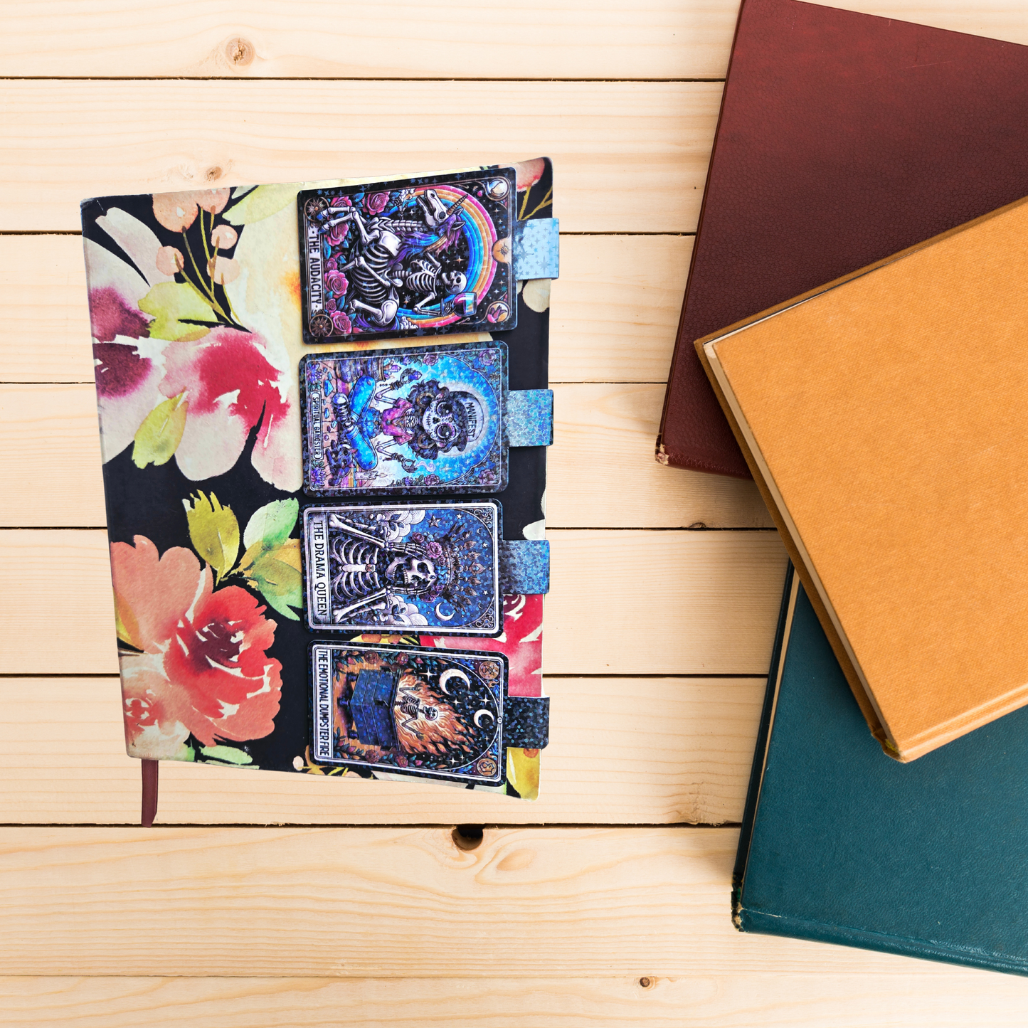 Floral design notebook with tarot card bookmarks on a wooden surface with other books.
