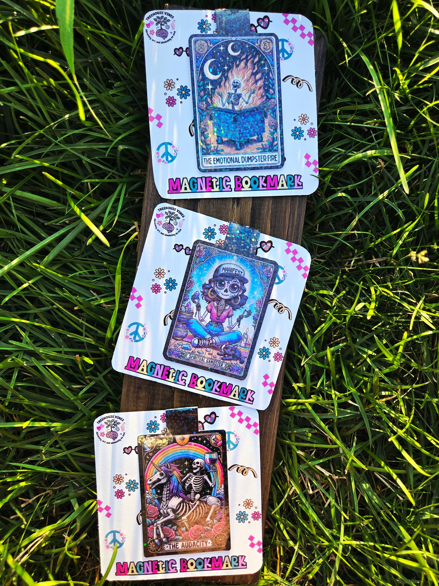 Three tarot card bookmarks with colorful designs and text on a wooden deck against a grass background.