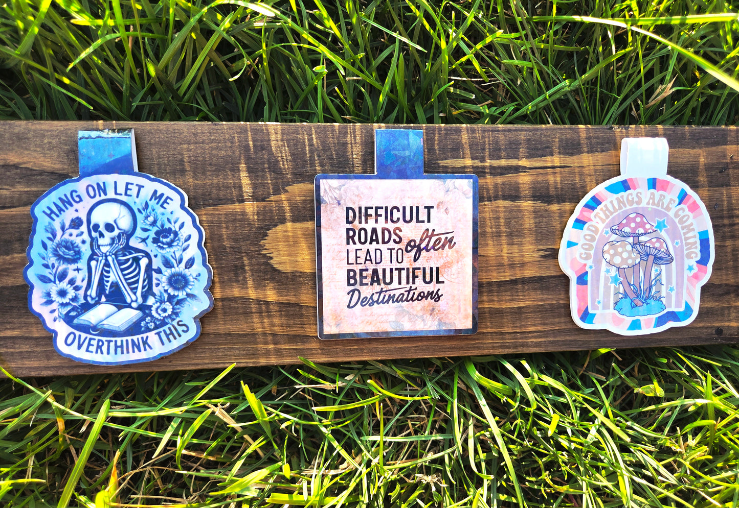 Three motivational bookmarks on a wooden board with grass in the background