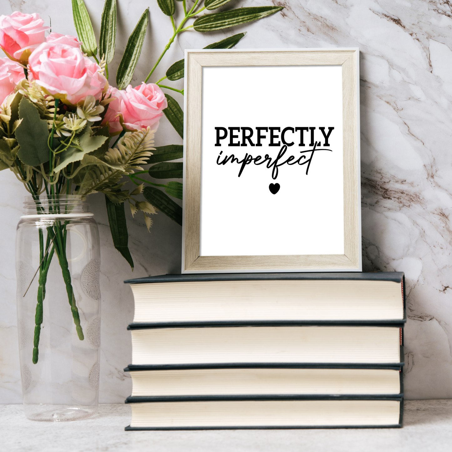 Framed print with 'PERFECTIONLY imperfect' text on a marble surface with flowers and books.