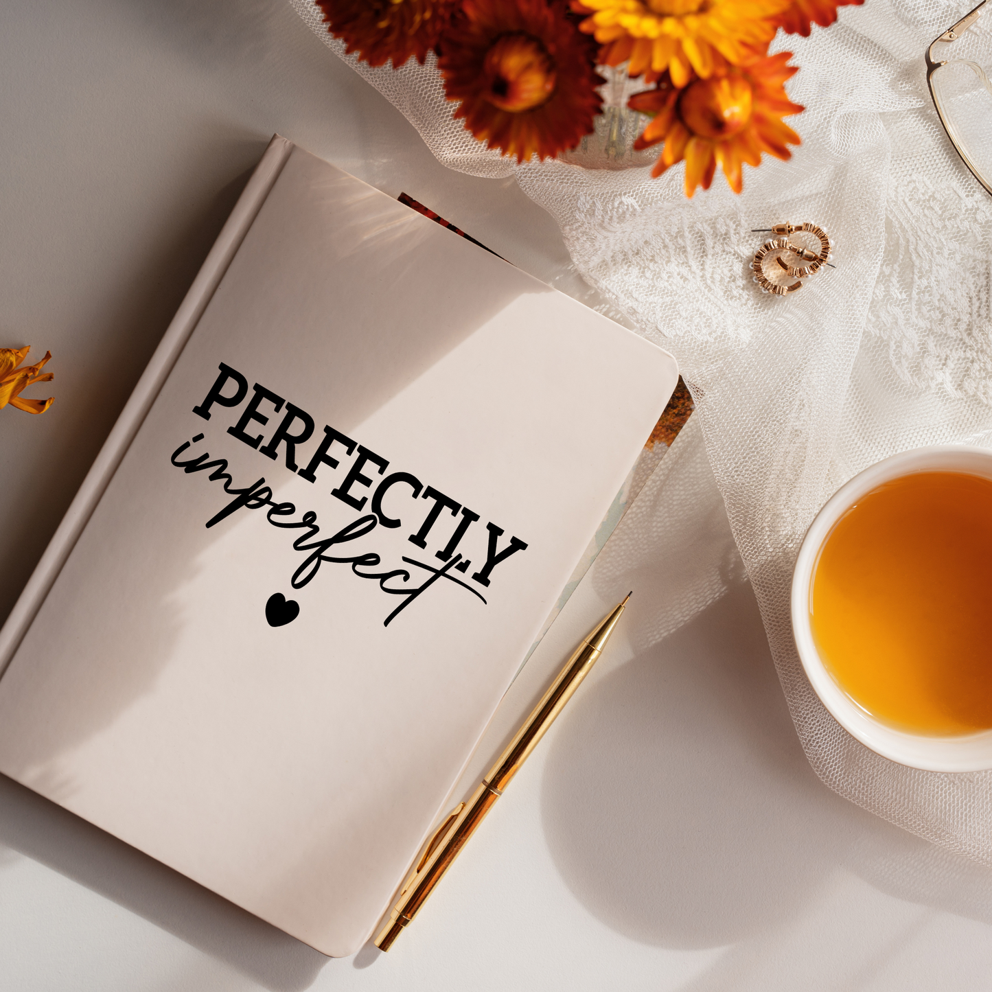 Open book with 'Perfectly imperfect' text, cup of tea, and flowers on a light surface