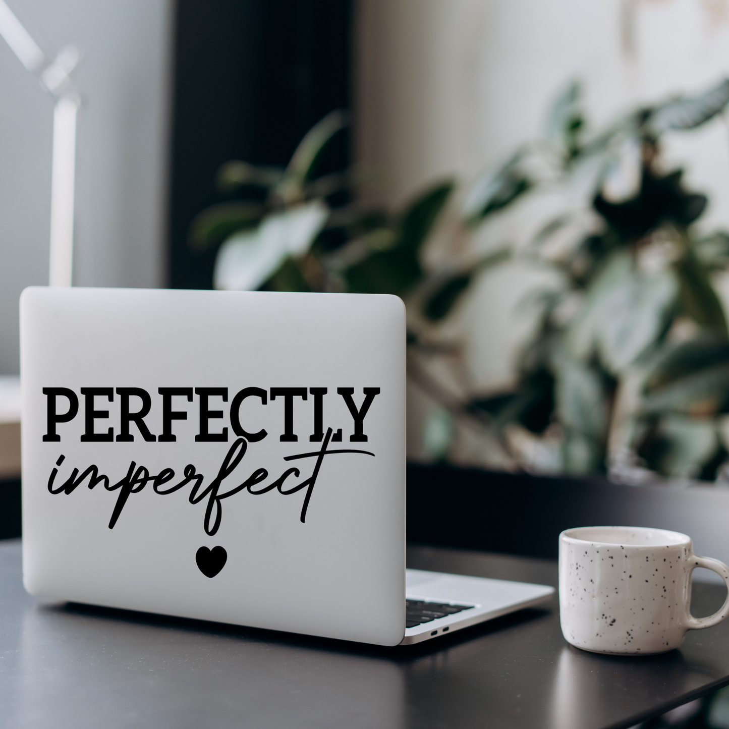 Laptop with a graphic design on a desk with a mug and plant in the background
