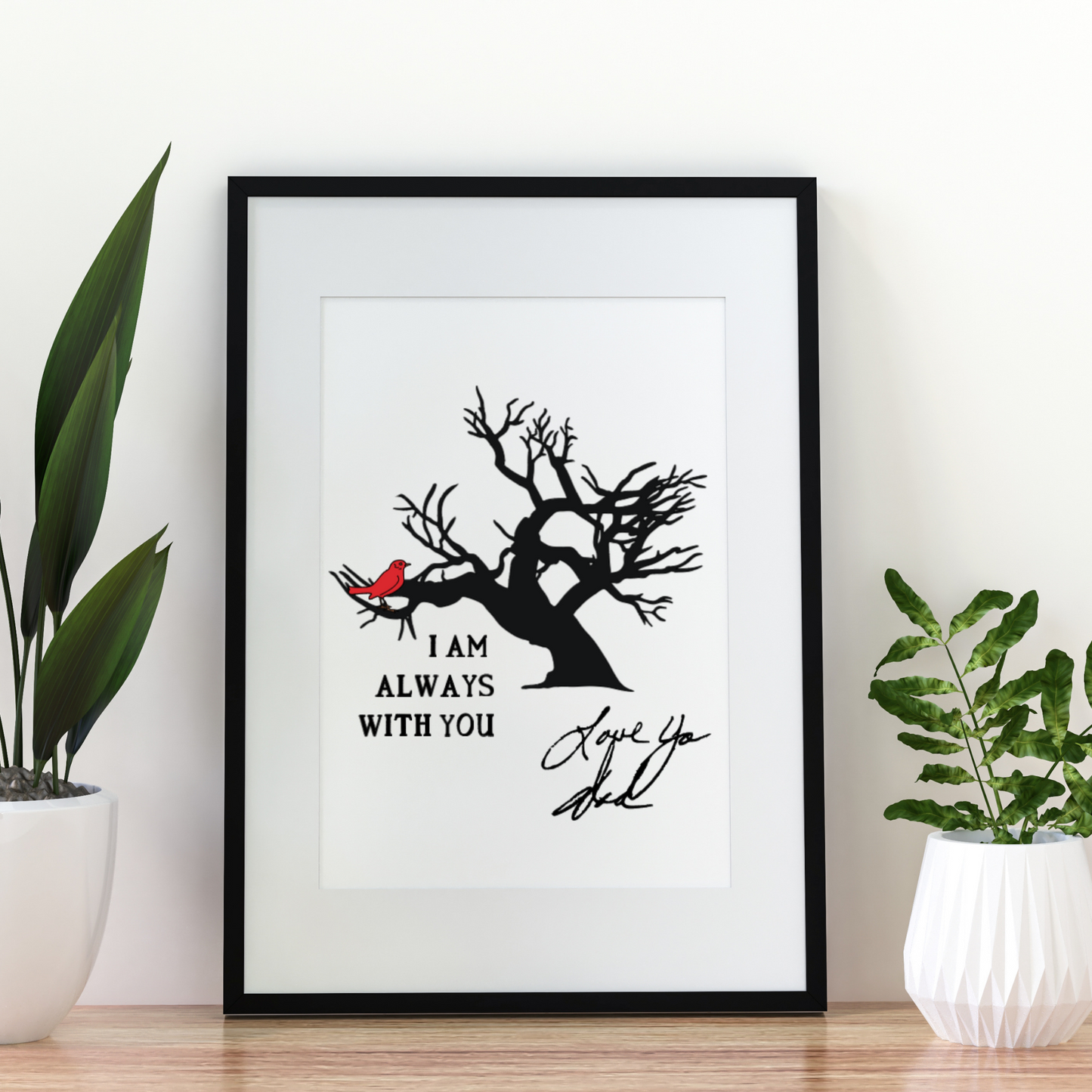 Minimalist framed print featuring a red cardinal on a bare tree with the message “I am always with you” and a handwritten “Love You Dad” signature, set against a white wall with green potted plants.