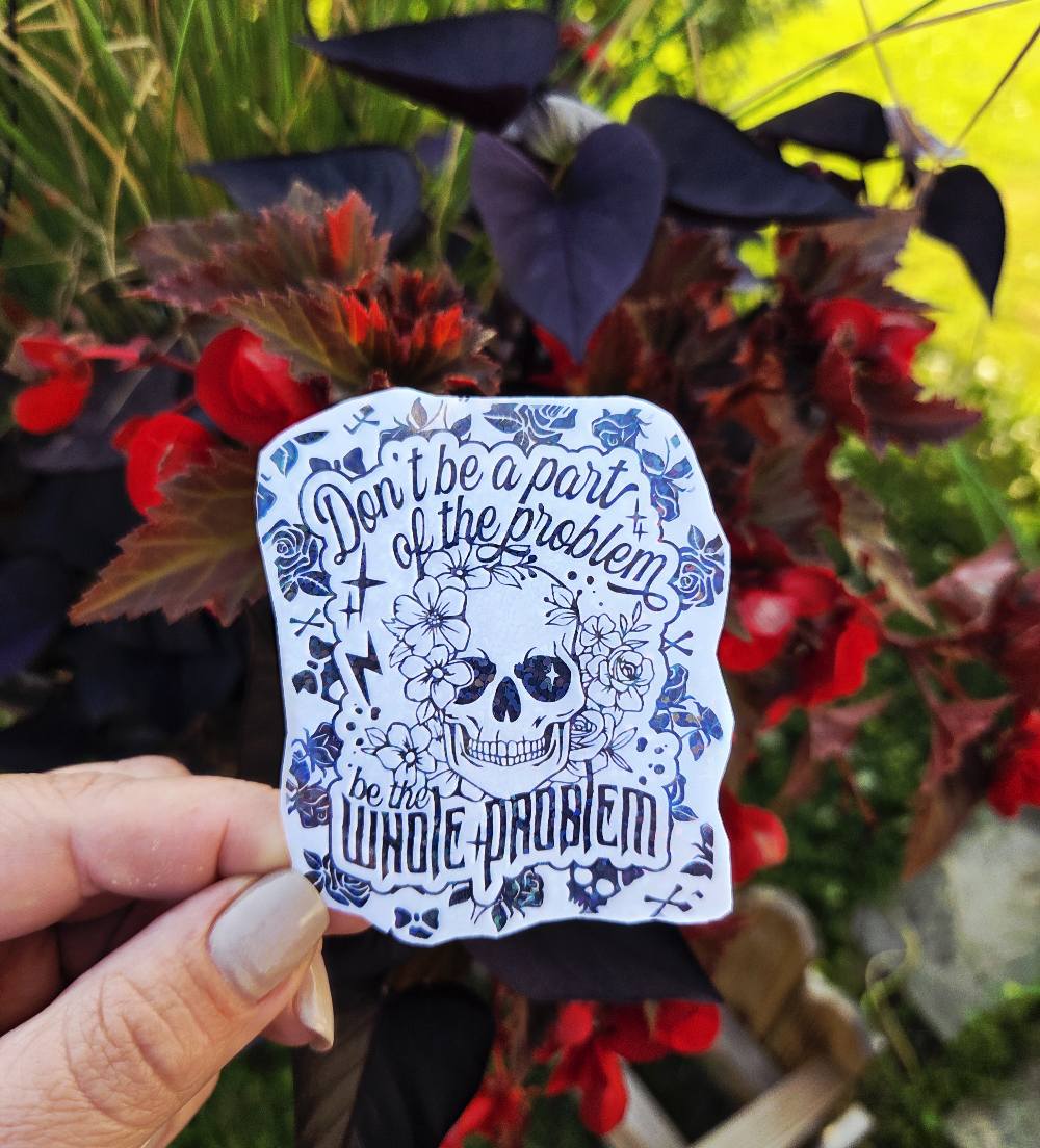 Black and white sticker of a skull surrounded by flowers with the phrase “Don’t be a part of the problem, be the whole problem”
