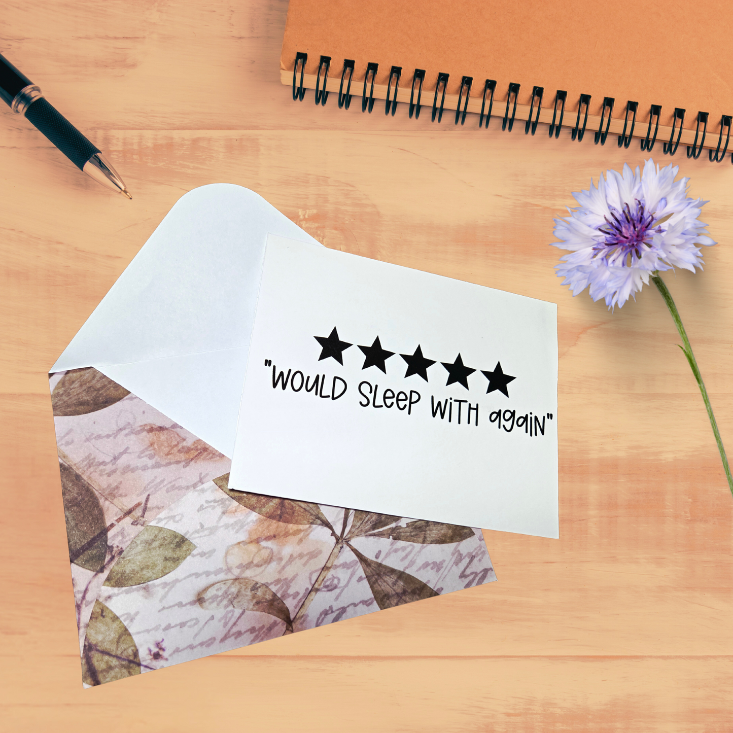 Note with 'Would sleep with again' text on a wooden surface with a pen and flower.