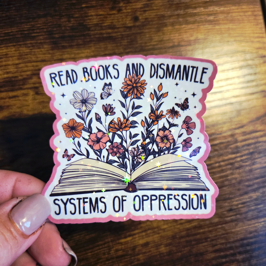 Sticker with an open book and floral design held by a hand on a wooden surface.