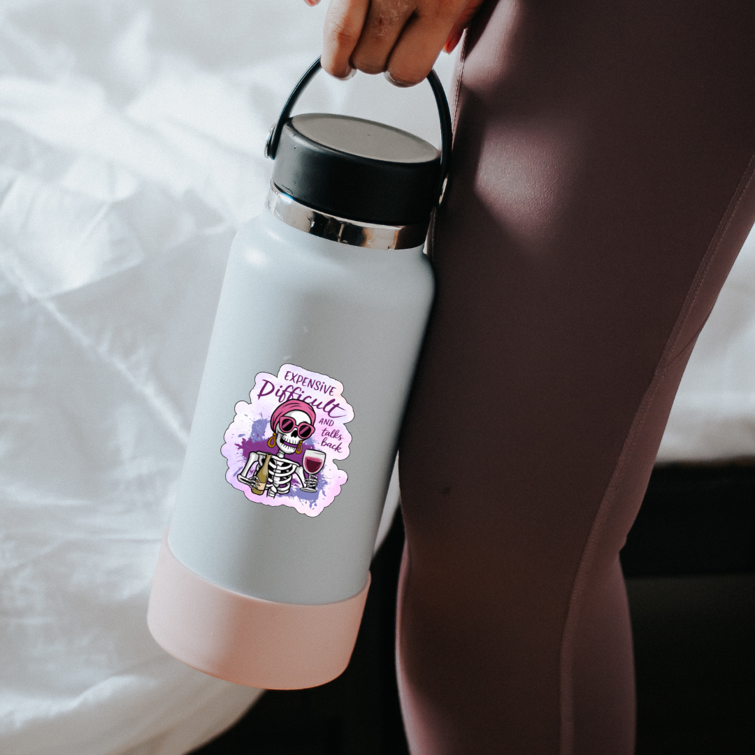 White water bottle with a pink base and handle, featuring a skeleton design and text, held by a person.