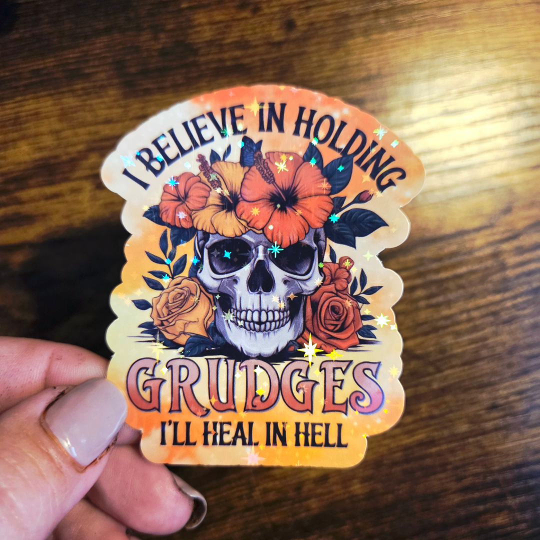 Sticker with skull design and text held by a hand on a wooden surface