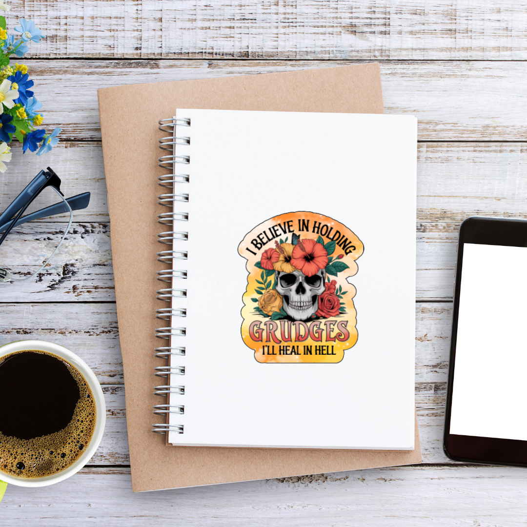 Notebook with a skull and flowers design on a wooden surface with coffee and flowers.