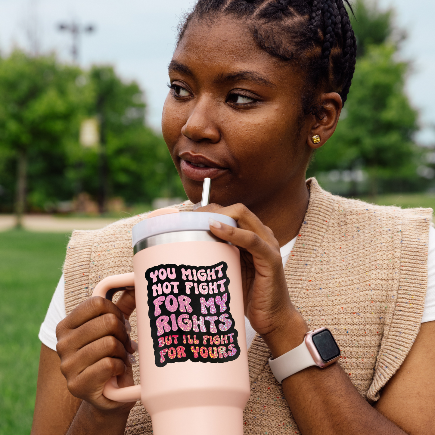 Woman drinking from a pink insulated mug with a quote in a park