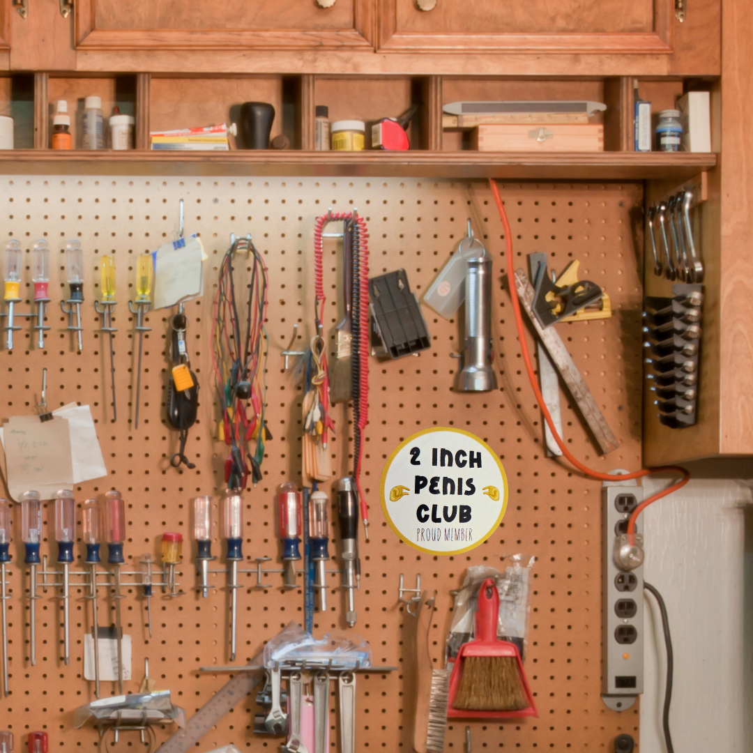 pegboard with tools and a humorous sign labeled '2 Inch Penis Club' in a workshop setting