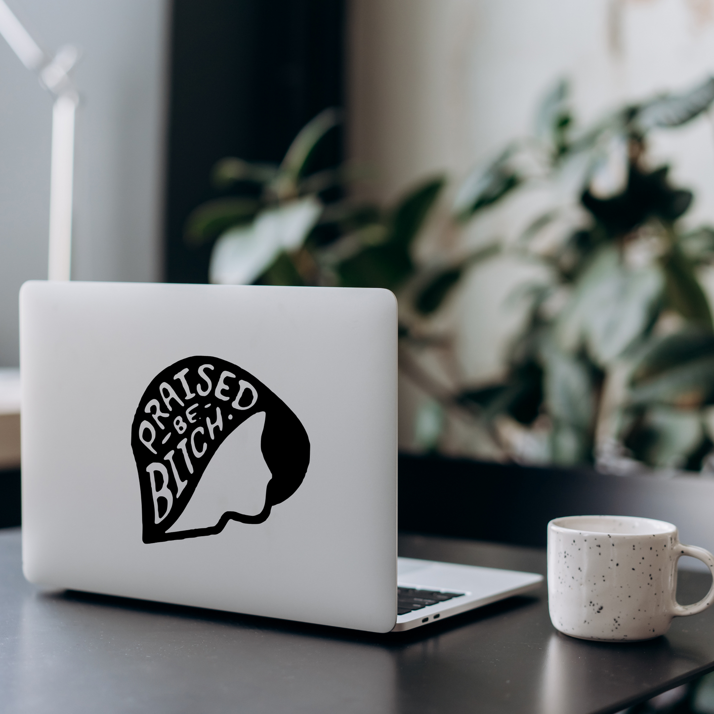 Laptop with a graphic design on a desk with a mug and plant in the background
