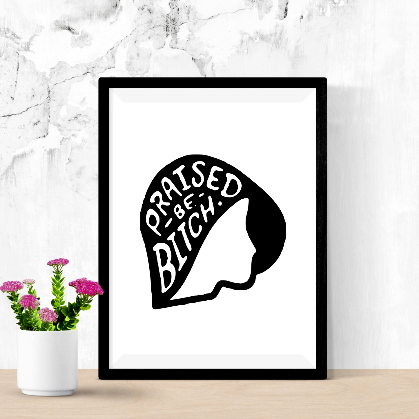 Framed artwork with a silhouette and text on a white wall with a plant below.
