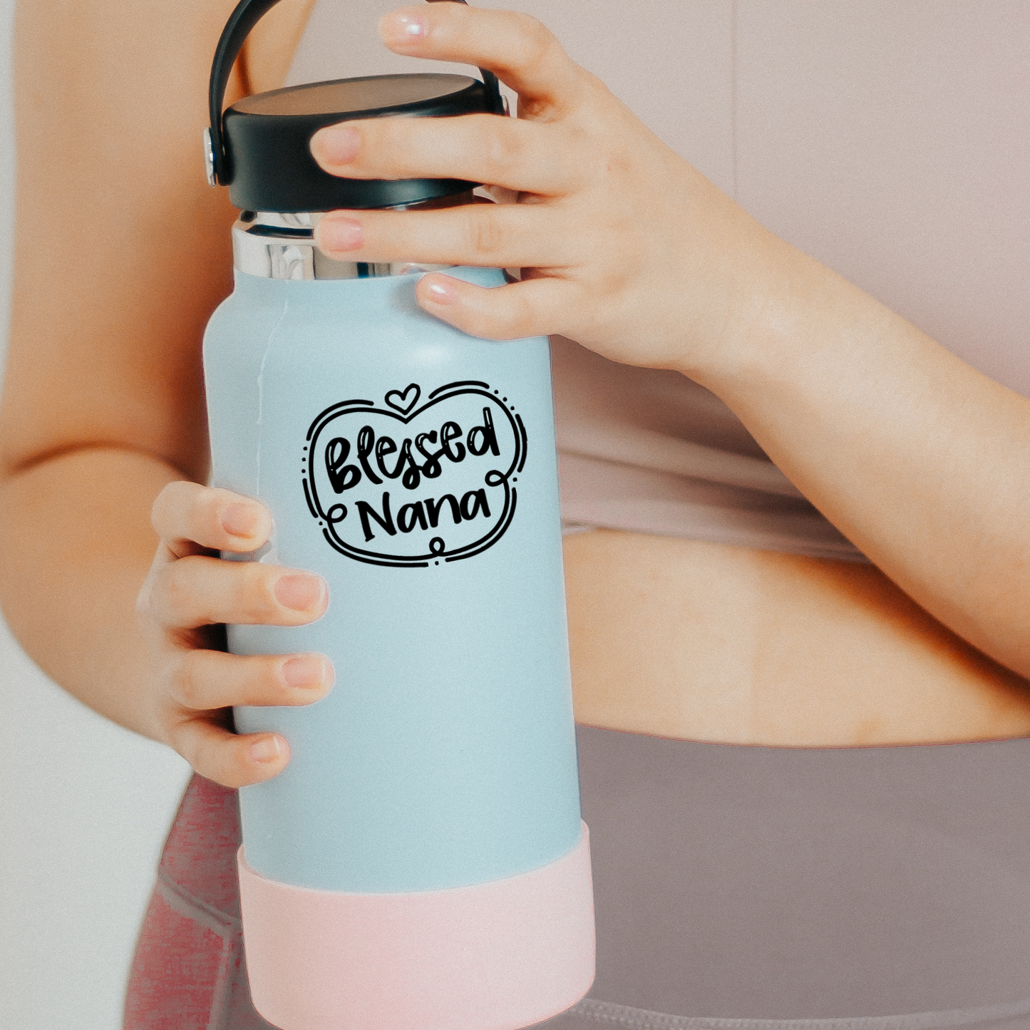 Black vinyl decal that reads “Blessed Nana” in playful hand lettering with heart and swirly border design