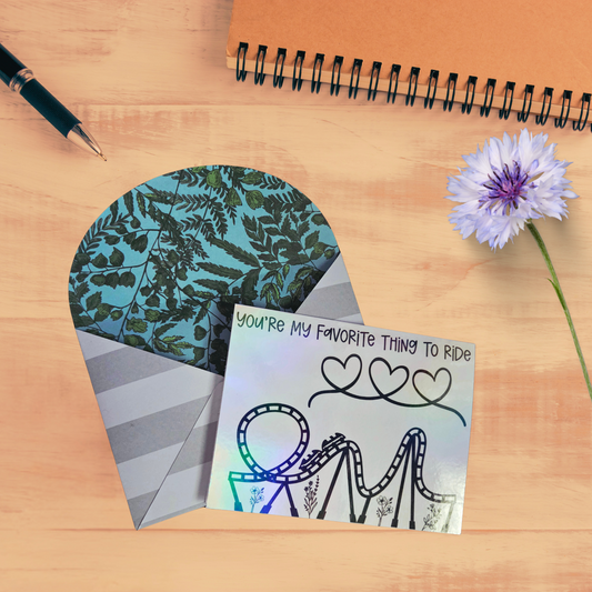 Card with roller coaster design and floral elements on a wooden surface