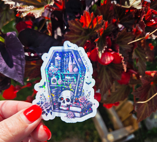 Sticker shaped like a coffin bookshelf with books, pink potion bottles, roses, and a skull, surrounded by bats and flowers. Text along the side reads “Never Trust the Living.”
