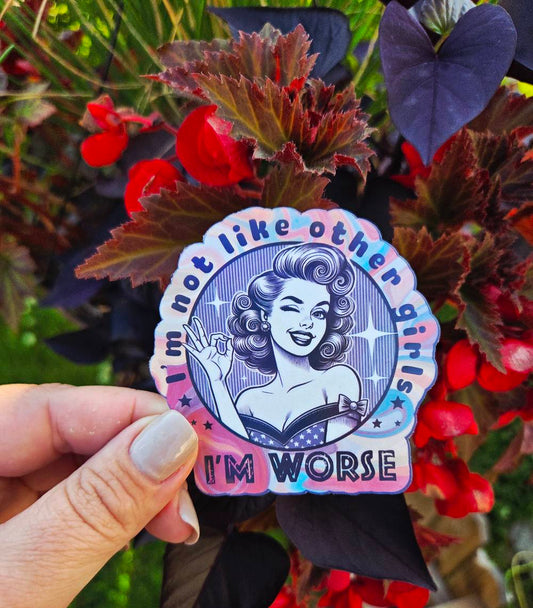 Sticker featuring a retro pin-up girl with curled hair, winking and giving an OK hand gesture, surrounded by the phrase “I’m not like other girls – I’m worse” on a colorful background