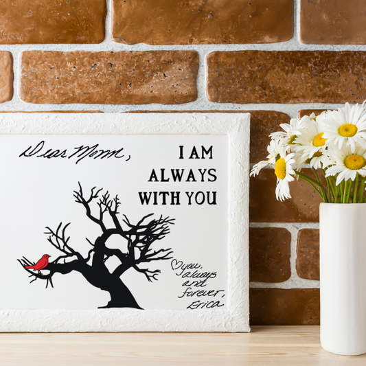 Framed memorial artwork with a black tree and red cardinal, featuring handwritten text that says “Dear Mom,” and “I am always with you. Love you, always and forever, Erica,” displayed on a wood shelf with a white vase of daisies against a brick wall.