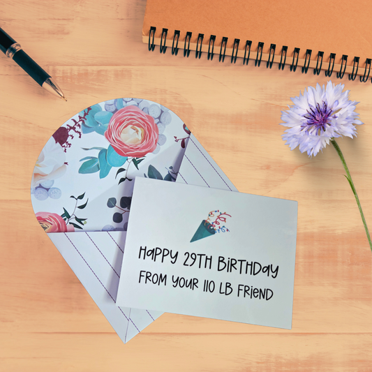 Birthday card with floral design and humorous message on a wooden surface with a pen and flower.