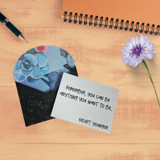 Motivational card with floral design and inspirational quote on a wooden surface with a pen and flower.