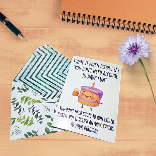 Greeting card with humorous message and envelope on a wooden surface with a pen and flower.