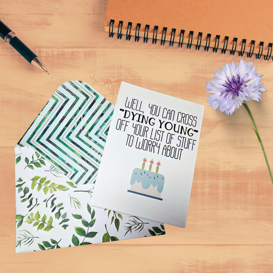 Greeting card with humorous birthday message on a wooden surface with a pen and flower.