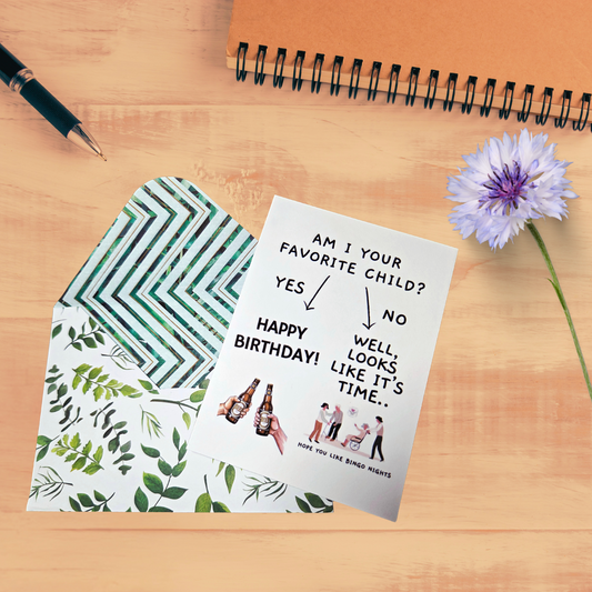 Birthday card with envelope on a wooden surface with a pen and flower.
