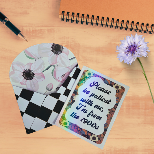Floral-patterned card with a humorous message on a wooden surface with a pen and flower.