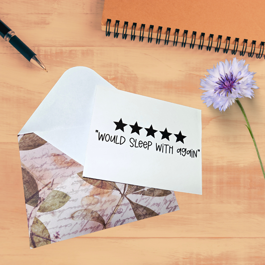 Note with 'Would sleep with again' text on a wooden surface with a pen and flower.