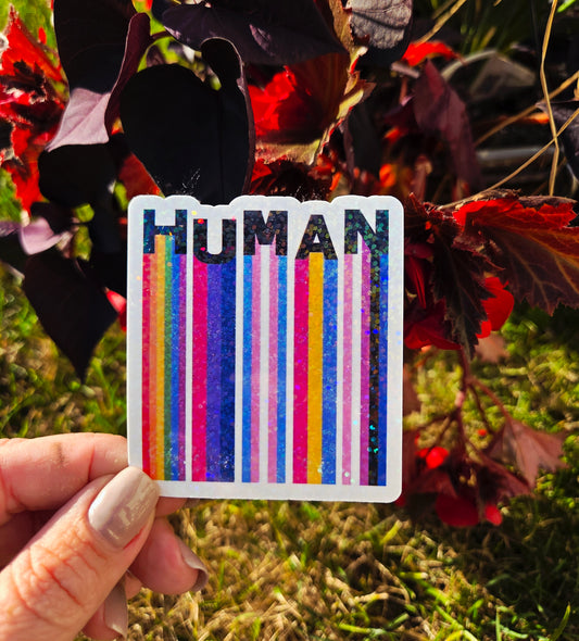 Square holographic sticker with rainbow barcode stripes and the word “HUMAN” in bold black text