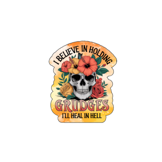 Holographic sticker with a floral-decorated skull and bright orange accents. Text reads “I Believe in Holding Grudges – I’ll Heal in Hell.”