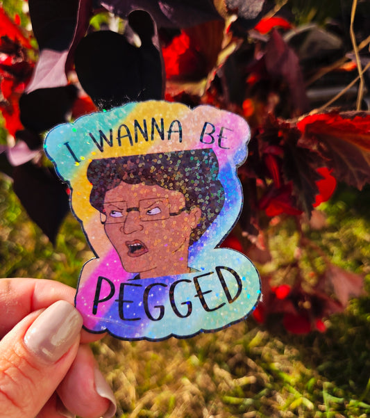 Holographic parody sticker with a cartoon woman and the phrase “I Wanna Be Pegged” in bold black lettering