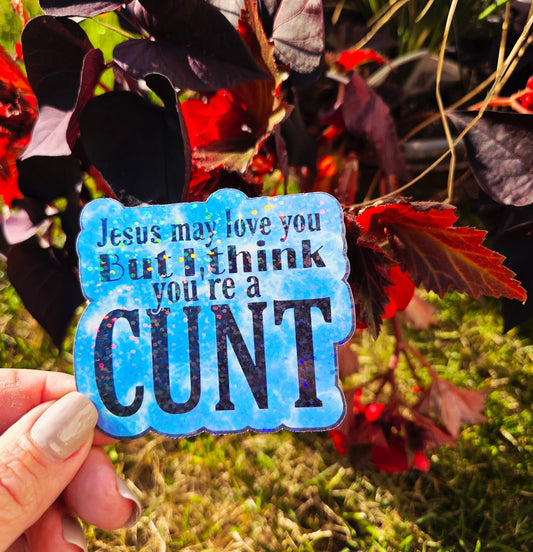 Holographic sticker that says “Jesus may love you but I think you’re a c*nt” in black text on a blue sparkle background