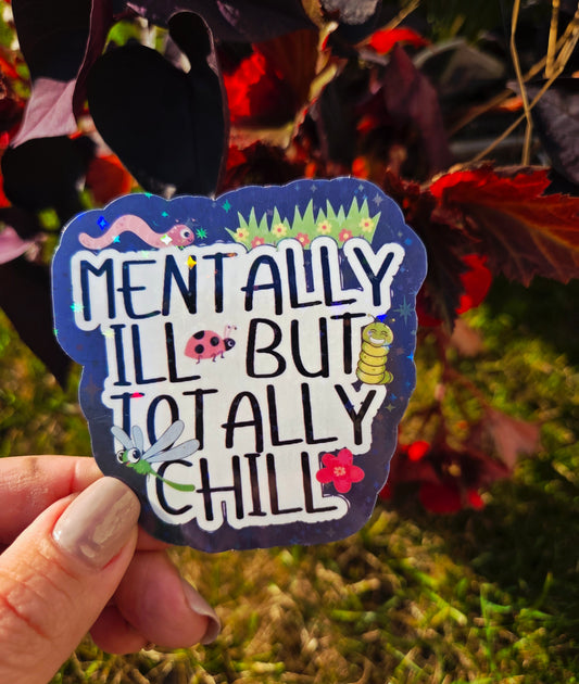 Holographic sticker that says “Mentally Ill But Totally Chill” with bugs, grass, and sparkles