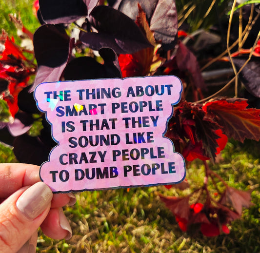 Holographic sticker with the quote “The thing about smart people is that they sound like crazy people to dumb people” in bold black lettering