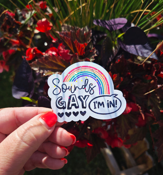 Vinyl sticker with rainbow arch and the phrase “Sounds Gay, I’m In!” in playful black font with five hearts beneath the word "Gay"