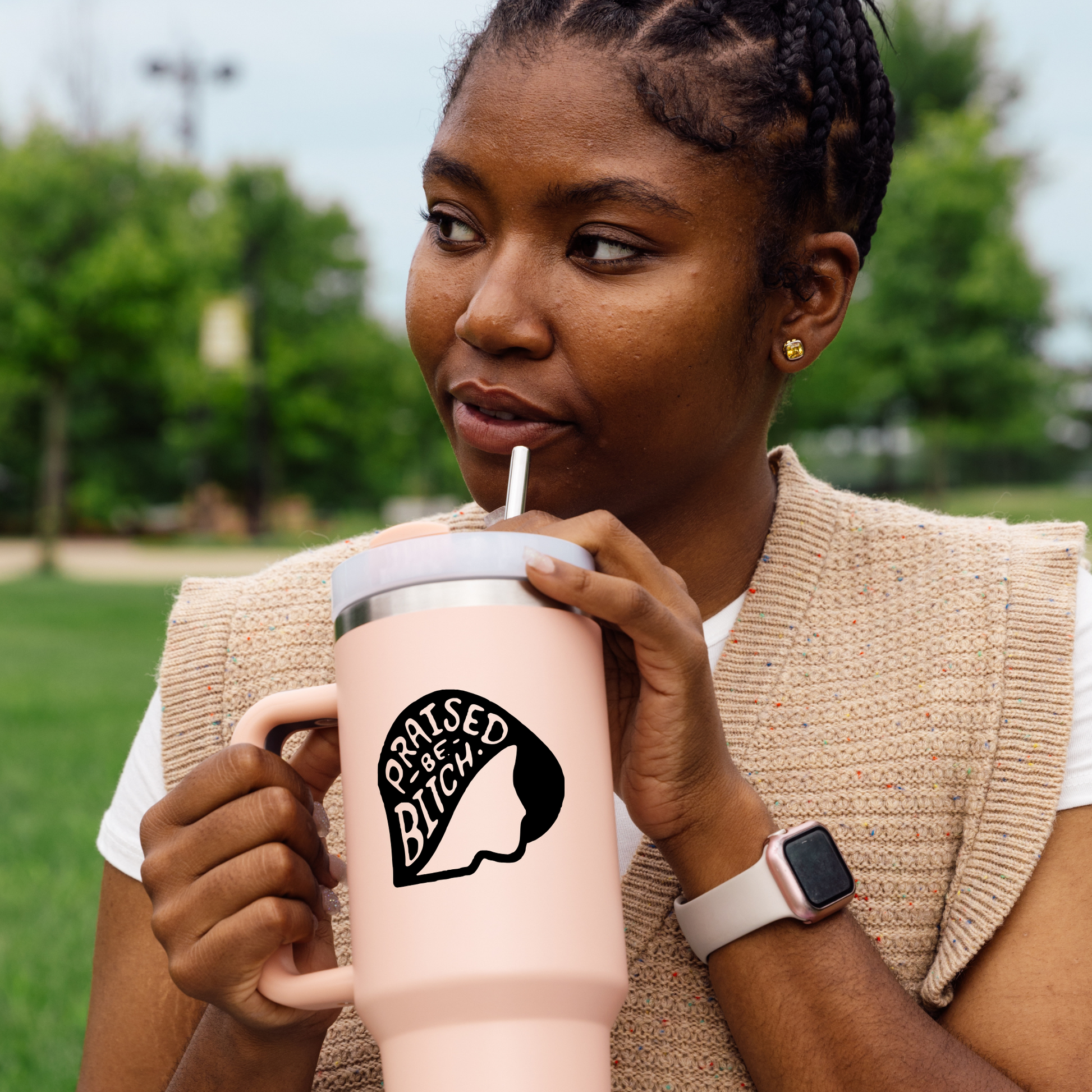 Woman drinking from a pink insulated tumbler with a graphic design outdoors