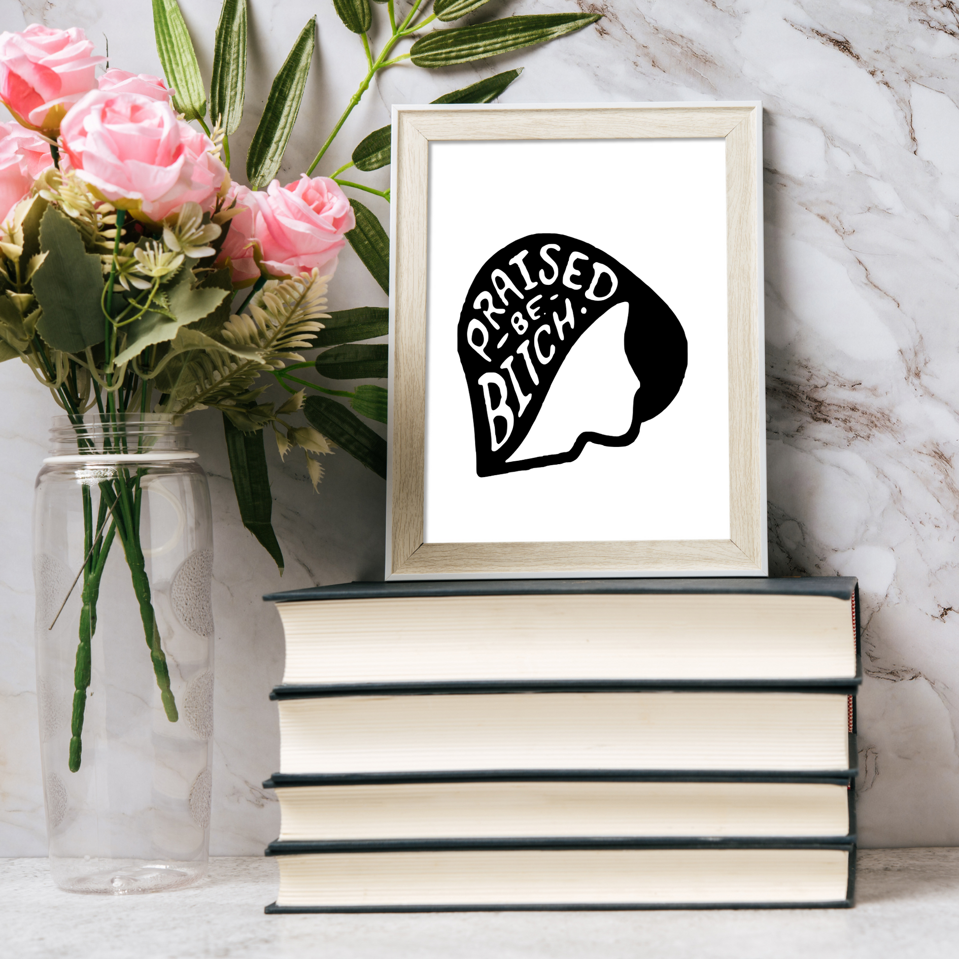 Framed artwork with a quote on a stack of books next to pink flowers.