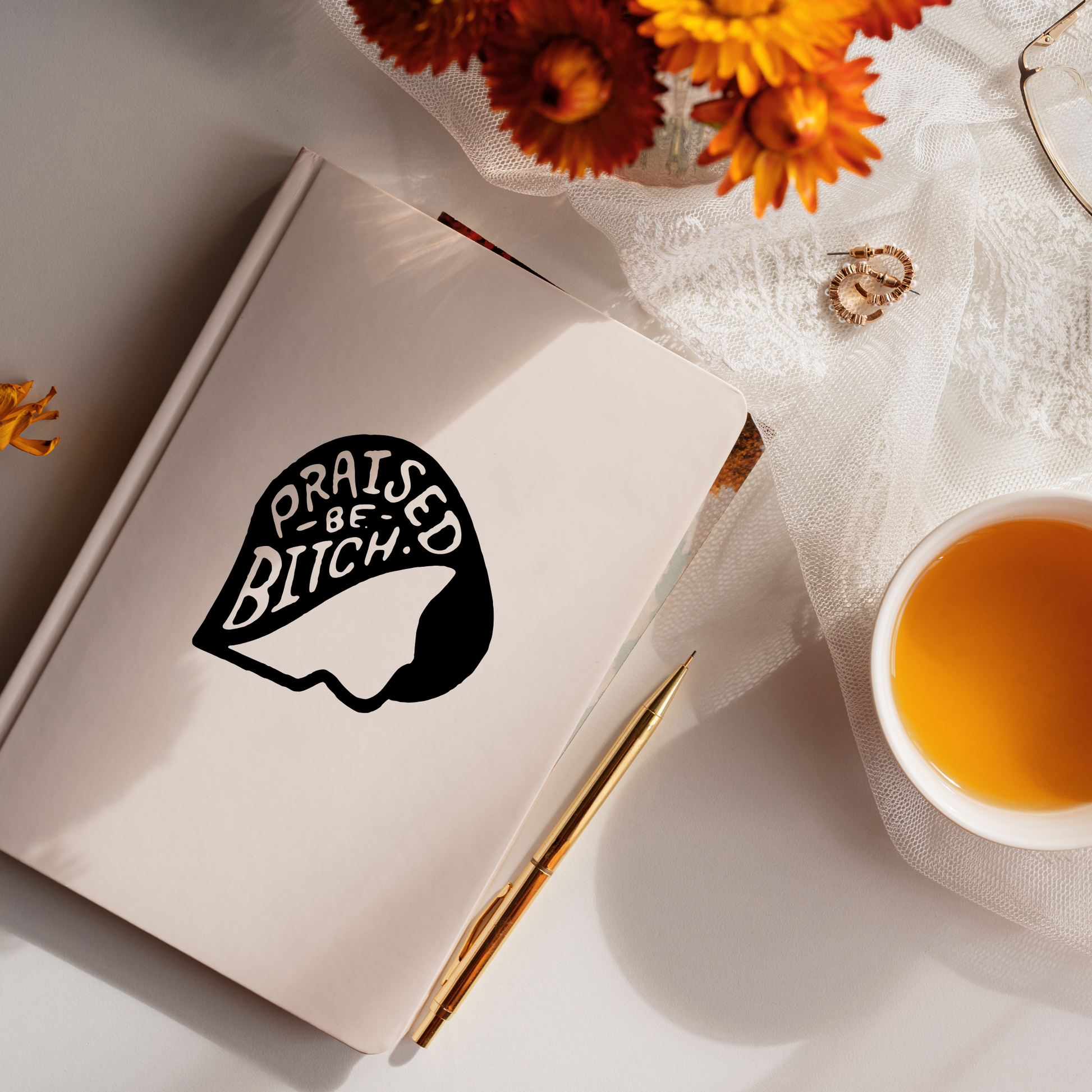 Notebook with a graphic design on a surface with flowers and a cup of tea.