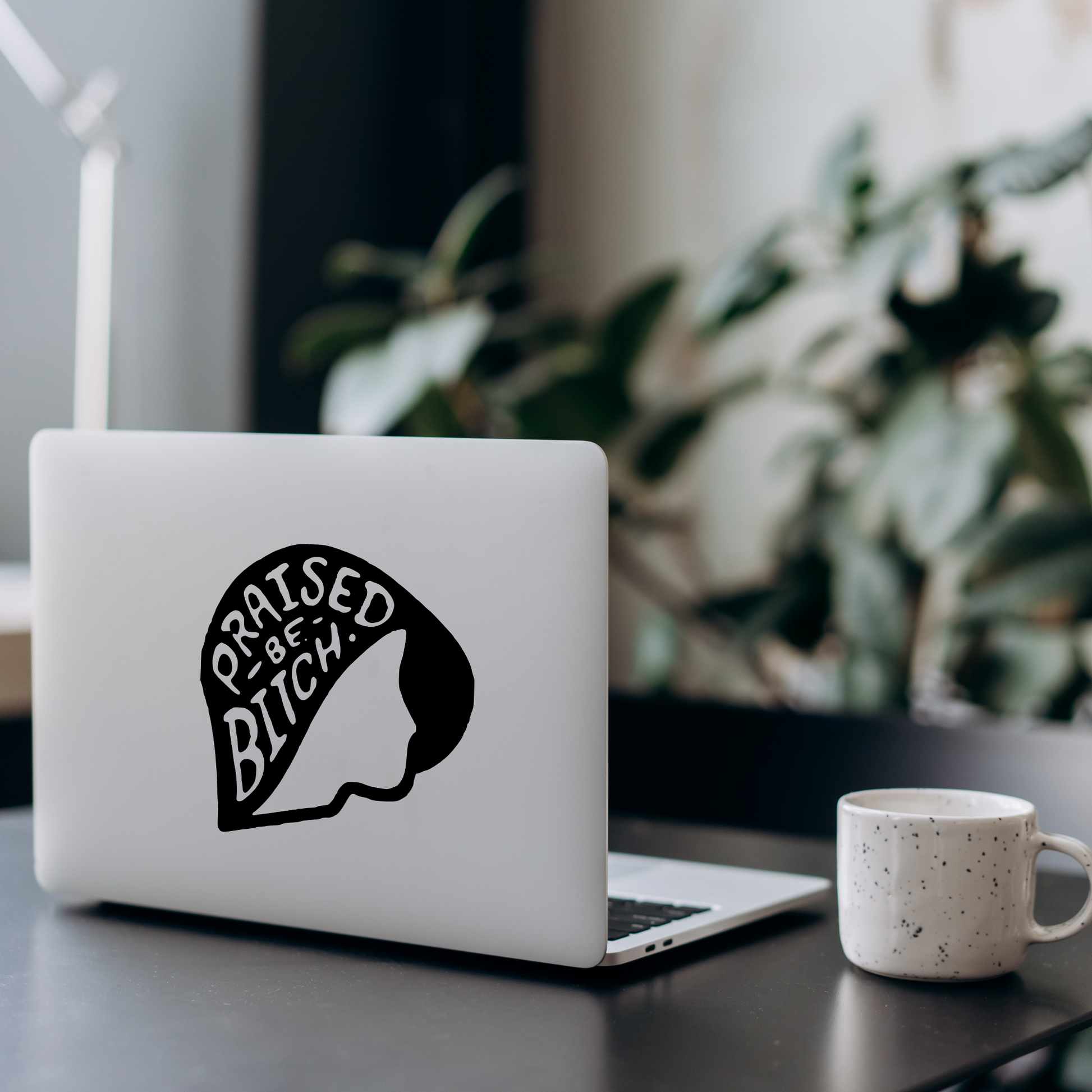 Laptop with a graphic design on a desk with a mug and plant in the background