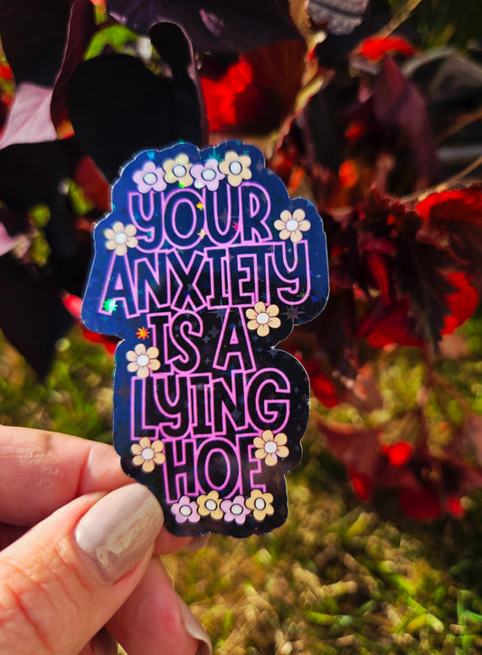 Holographic mental health sticker with the quote “Your Anxiety Is a Lying Hoe” in purple and white with flower doodles