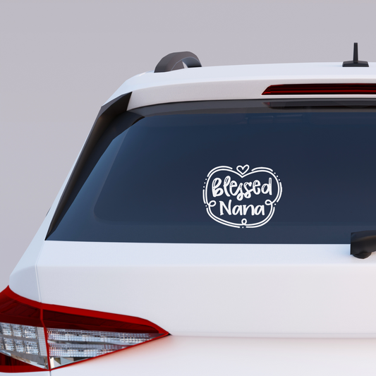 Black vinyl decal that reads “Blessed Nana” in playful hand lettering with heart and swirly border design